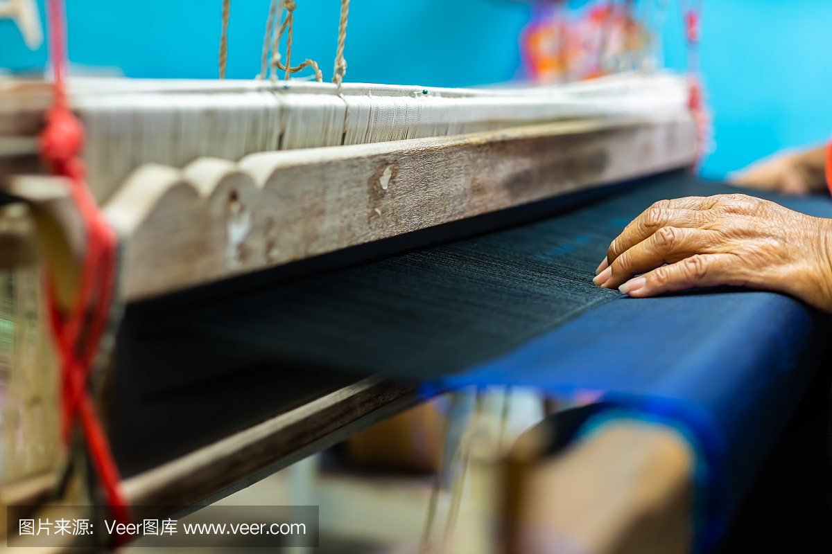 纺织机上女工的手和泰国传统丝绸的特写。用于自制丝绸纺织品的织布机